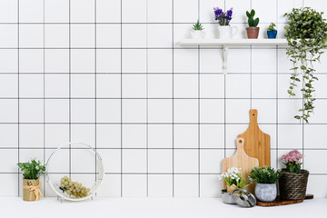 Various kinds of kitchen tools arranged on the white table. And tidy flower pots are placed neatly on the shelf.