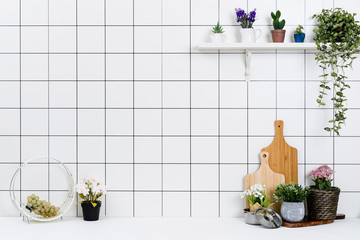 Various kinds of kitchen tools arranged on the white table. And tidy flower pots are placed neatly on the shelf.