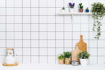 Various kinds of kitchen tools arranged on the white table. And tidy flower pots are placed neatly on the shelf.