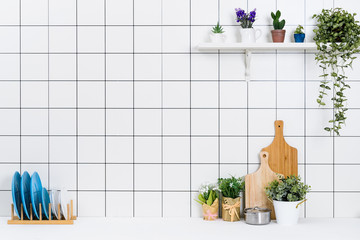 Various kinds of kitchen tools arranged on the white table. And tidy flower pots are placed neatly on the shelf.