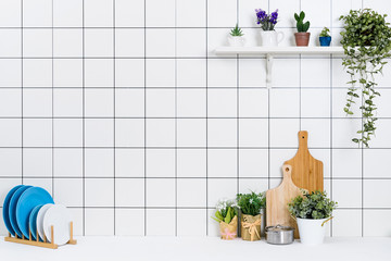 Various kinds of kitchen tools arranged on the white table. And tidy flower pots are placed neatly on the shelf.