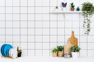 Various kinds of kitchen tools arranged on the white table. And tidy flower pots are placed neatly on the shelf.