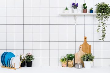 Various kinds of kitchen tools arranged on the white table. And tidy flower pots are placed neatly on the shelf.