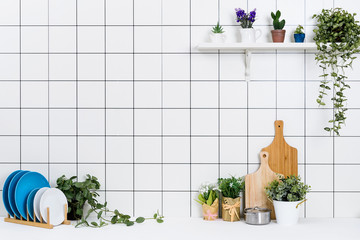 Various kinds of kitchen tools arranged on the white table. And tidy flower pots are placed neatly on the shelf.