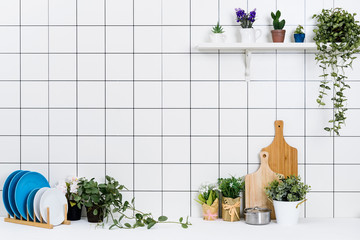 Various kinds of kitchen tools arranged on the white table. And tidy flower pots are placed neatly on the shelf.