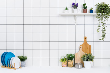 Various kinds of kitchen tools arranged on the white table. And tidy flower pots are placed neatly on the shelf.