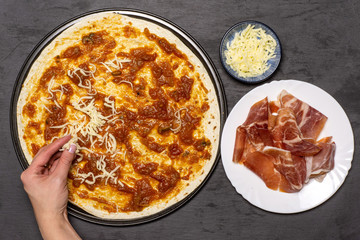Woman hand is sprinkling pizza with a cheese. recipe step by step pizza capricciosa flatlay on grey stone