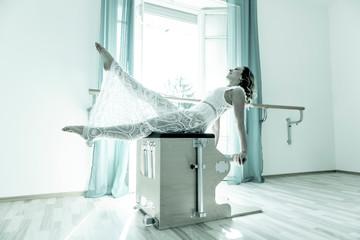 Woman Exercising on Pilates Machine Against a Window With Sunlight in Switzerland.