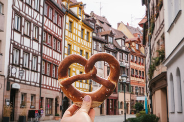A girl holds in her hand a traditional German pretzel on the background of a beautiful architecture or street in Nuremberg in Germany. - obrazy, fototapety, plakaty