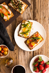Breakfast table with tasty bruschetta crostini toasts, cream cheese, fresh vegetables and fruits and a cup of black coffee. Morning heathy balanced diet. Colorful ingredients on rustic wood background