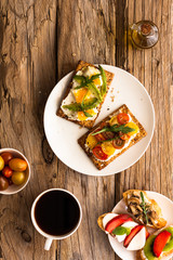 Breakfast table with tasty bruschetta crostini toasts, cream cheese, fresh vegetables and fruits and a cup of black coffee. Morning heathy balanced diet. Colorful ingredients on rustic wood background