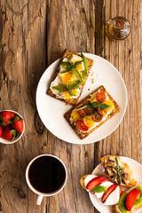 Breakfast table with tasty bruschetta crostini toasts, cream cheese, fresh vegetables and fruits and a cup of black coffee. Morning heathy balanced diet. Colorful ingredients on rustic wood background