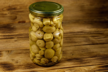 Delicious marinated mushrooms in glass jar on wooden table