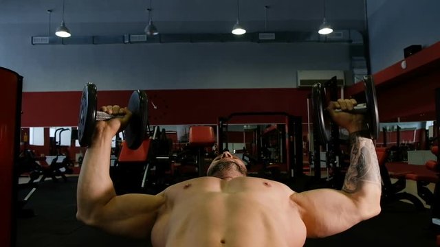 Muscular man in the gym lifts weights lying on a bench