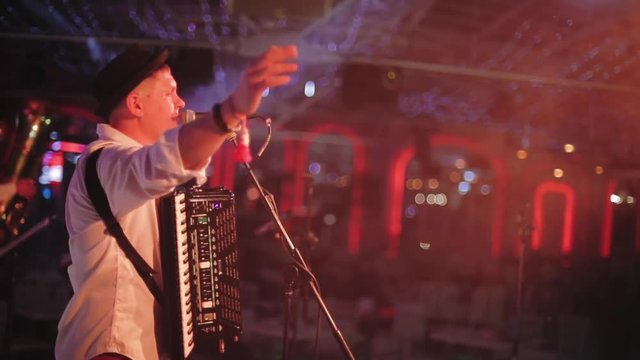 Man singing to microphone on blur background /  hipster with accordion. Unrecognizable male person in color shirt, Balkan singer concert on stage