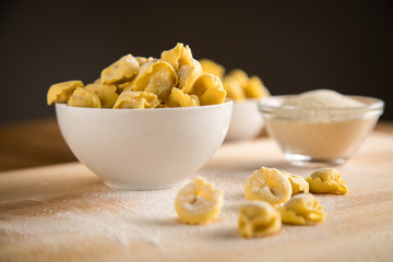 Frische, rohe Cappelletti Tortellini Pasta mit Mehl und Grieß in Porzellan Schale auf Holz Brett
