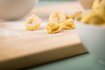 Frische, rohe Cappelletti Tortellini Pasta mit Mehl und Grieß in Porzellan Schale auf Holz Brett und Pastell Grün Hintergrund