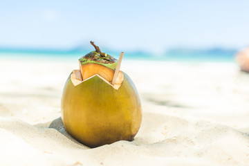 Fresh young coconut lying on the sand beach background with straw ready for drink.