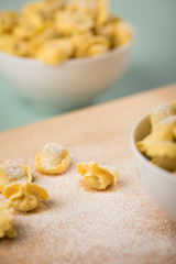 Frische, rohe Cappelletti Tortellini Pasta mit Mehl und Grieß in Porzellan Schale auf Holz Brett und Pastell Grün Hintergrund