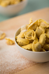 Frische, rohe Cappelletti Tortellini Pasta mit Mehl und Grieß in Porzellan Schale auf Holz Brett und Pastell Grün Hintergrund