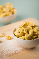 Frische, rohe Cappelletti Tortellini Pasta mit Mehl und Grieß in Porzellan Schale auf Holz Brett und Pastell Grün Hintergrund