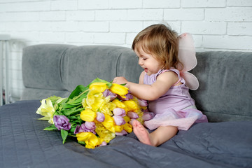 The little girl with tulips in fairy clothes sits on a bed. Spring mood