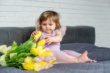The little girl with tulips in fairy clothes sits on a bed. Spring mood