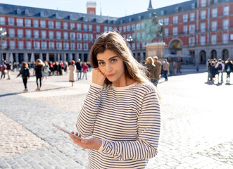 Young woman looking at smart mobile phone in Plaza Mayor Madrid feeling lost looking for directions