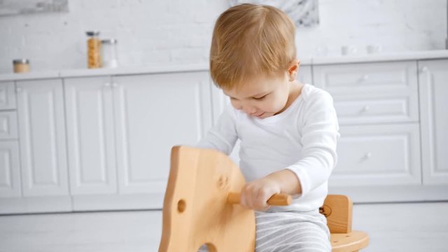 cute toddler boy laughing and riding wooden rocking horse at home 