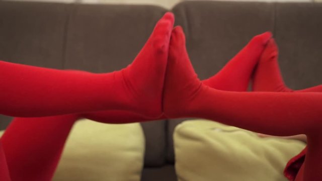Two little girls in red tights playing in bed, pushing each other's legs