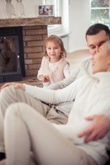 The family sits on the couch near the fireplace. Mom, Dad, daughter in the home interior. Cozy.