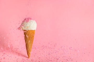 summer creative concept with ice cream cone and dynamic strewing pink sprinkles on background,...