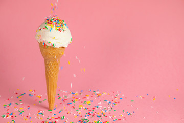 summer creative concept with ice cream cone and dynamic strewed sprinkles on pink background
