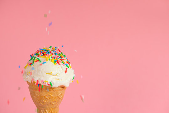 close up of creative concept with ice cream cone and dynamic strewed sprinkles on pink background