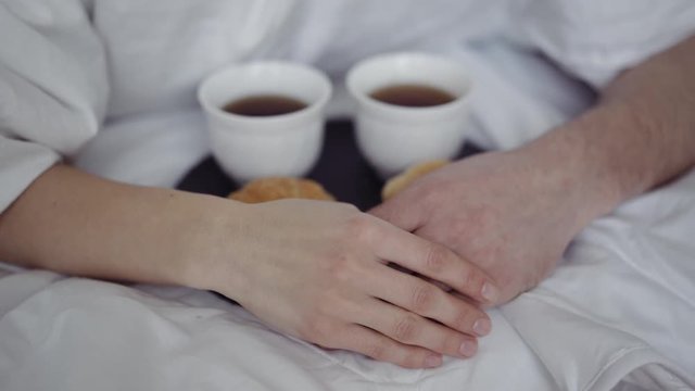 breakfast with coffee and fresh croissants, on table, happy couple hiding under a blanket and hold hands. Happy morning
