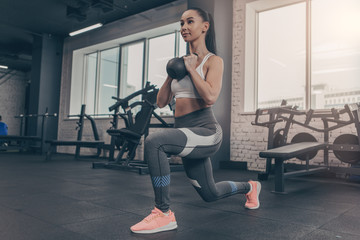 Fototapeta na wymiar Low angle shot of a sporty young woman doing lunges with kettlebell. Attractive sportswoman enjoying working out at the gym, copy space. Fitness female in sportswear training with weights
