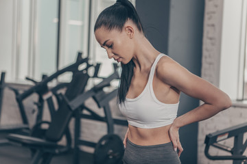 Beautiful athletic woman having backache after workout at the gym. Attractive fitness female having...