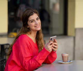 Attractive young woman using smart mobile phone sitting in a coffee shop outside terrace
