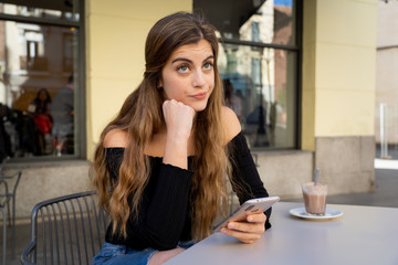 Attractive young woman sitting bored in a coffee shop using smart mobile phone feeling disappointed
