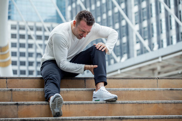 fitness man have knee pain sitting on steps of stair in the city. sport injury leg of run in urban...