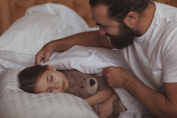 Loving father tucking blanket for his lovely little daughter. Adorable girl sleeping in bed,...