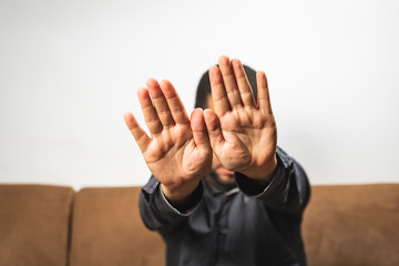 Serious young man sitting on sofa and showing stop gesture - hand gesture hide face stop sign