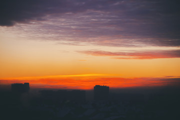 Cityscape with wonderful varicolored fiery dawn. Amazing dramatic multicolored cloudy sky. Dark silhouettes of city building roofs. Atmospheric background of sunrise in overcast weather. Copy space.