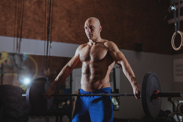 Fototapeta na wymiar Shirtless muscular mature crossfit athlete working out at the gym, lifting heavy barbell, copy space. Ripped sportsman weighlifting at crossfit box gym