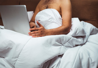 Young man is sitting in bed and watching movie on laptop