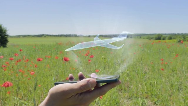 Hologram of small business jet aircraft on a smartphone. Person activates holographic image on the phone screen on the field with blooming poppies