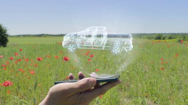 Hologram of pickup truck on a smartphone. Person activates holographic image on the phone screen on the field with blooming poppies