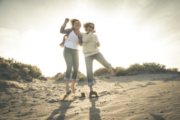 Friendship, summer vacation, freedom, happiness and people concept - two happy female middle age friends dancing and jumping on beach. Full-length shot of smiling curly girl in denim pants.