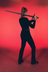Woman standing with sword against red background.