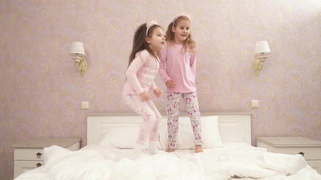 Little cute girls jumping on the bed in pink pajamas